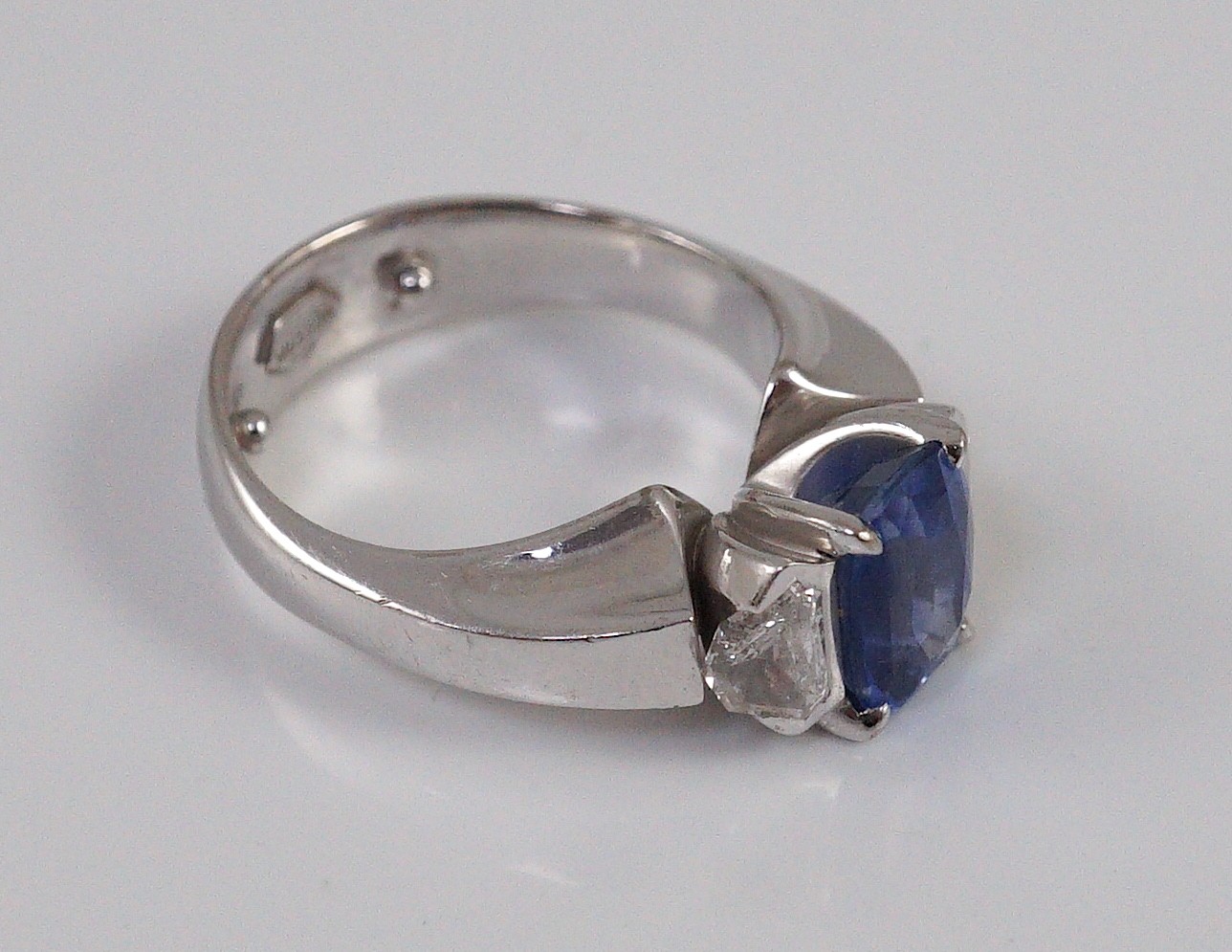 A modern white gold (tests as 18ct), single stone oval cut Ceylon sapphire and two stone shield cut diamond set dress ring, by Musson